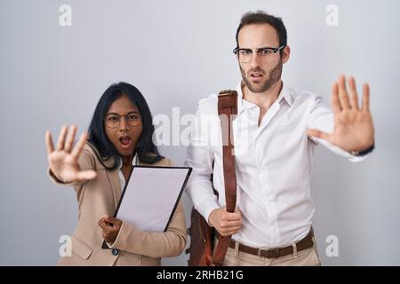 Interracial business couple wearing glasses doing stop gesture with hands palms, angry and frustration expression Stock Photo