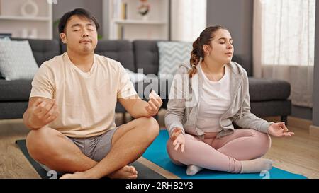 Man and woman couple sitting on floor doing yoga exercise at home Stock Photo
