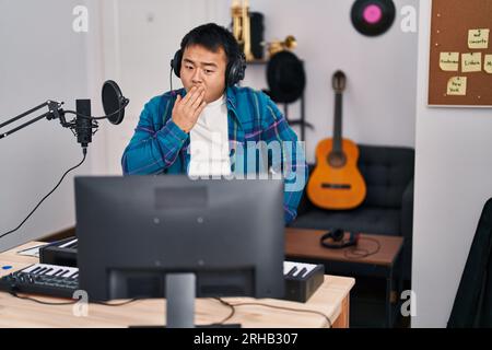 Young chinese man looking at online music tutorial covering mouth with hand, shocked and afraid for mistake. surprised expression Stock Photo