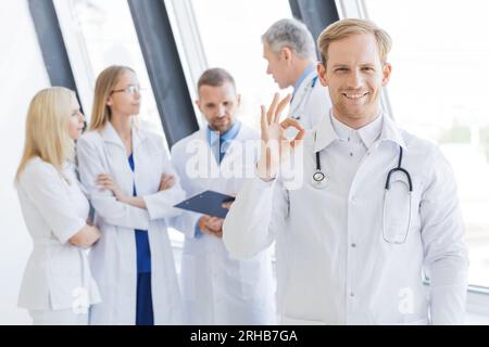 Team of medical professionals, young doctor looking at camera, smiling, showing ok sign Stock Photo