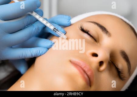 The doctor cosmetologist makes the rejuvenating facial injections procedure for anti wrinkles effect in a beauty salon. Stock Photo