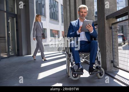 Executive business man in wheelchair with tablet using mobile device for work outdoors. Stock Photo