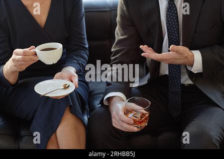 Closeup of two business partners discussing deal over drinks in office, focus on male hands holding glass of whiskey, copy space Stock Photo