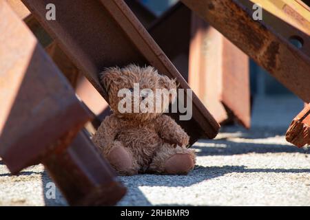 A teddy bear lies next to an anti-tank hedgehog on a road in the city of Dnipro in Ukraine during wartime Stock Photo