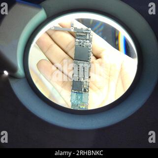 technician using magnifying glass smartphone motherboard Stock Photo