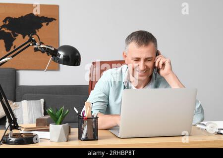 Mature male freelancer talking by mobile phone at table in office Stock Photo