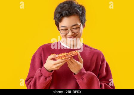 Young Asian man with tasty pizza on yellow background Stock Photo