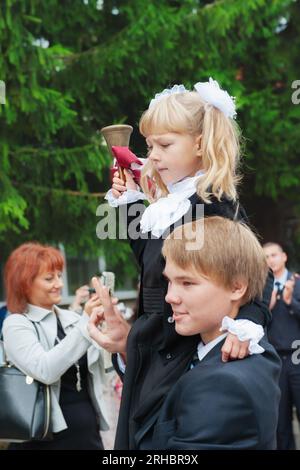 Kolomna, Moscow region, Russia. September 01, 2014 Traditional school first and last bell. A student carries a first-grader with a bell on his shoulde Stock Photo