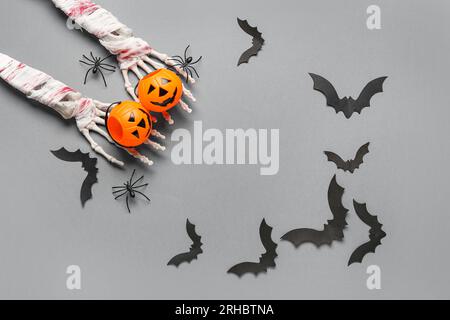 Frame made of skeleton hands, pumpkins, paper bats and spiders for Halloween celebration on grey background Stock Photo