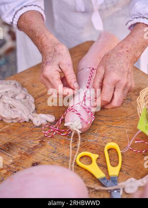 High angle of crop anonymous mature person in sterile uniform tying freshly filled raw sausage with thread standing at wooden table in butchery Stock Photo