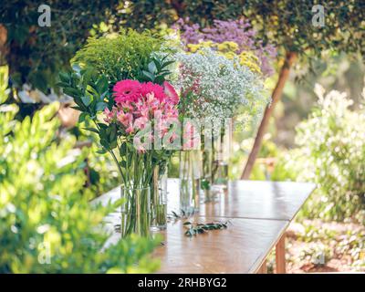 From above of bunches of various fresh multicolored flowers placed in vases on wooden table in green garden in sunlight Stock Photo