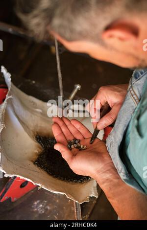 High angle of crop anonymous male worker putting little metal pieces into mold for welding while working in professional workshop Stock Photo