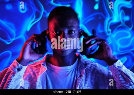 Concentrated African American male putting on headset in dark room with glowing vivid neon illumination and looking at camera Stock Photo