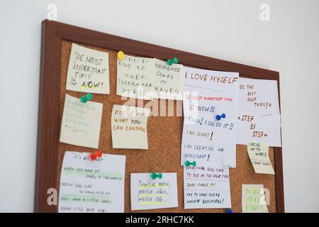 Cork board with stick notes with motivational sentences on them on a white wall. Motivational quotes written on stick notes pinned on cork board Stock Photo