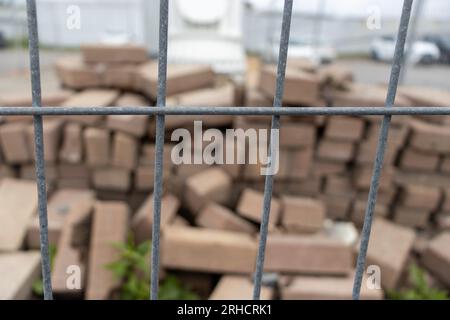 Chain link fence - pile of bricks - broken and stacked - overcast sky - car in background Stock Photo