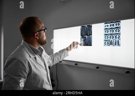 Side view of doctor studying MRI results. Male specialist working in clinic, carrying out description of the radiographs of a patient, pointing by pen. Concept of medicine and healthcare. Stock Photo