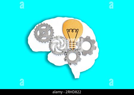 Close-up of a human brain outline with wooden gears and lightbulb isolated on a blue background. Stock Photo