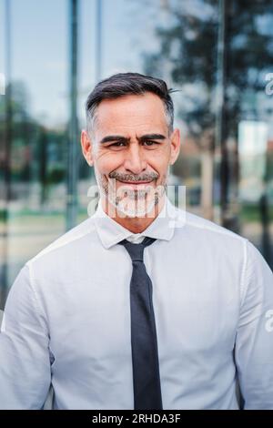 Vertical portrait of successful mature caucasian business man smiling looking at camera standing outdoors at workplace with cheerful attitude. Front view of handsome executive employee wearing a suit. High quality photo Stock Photo