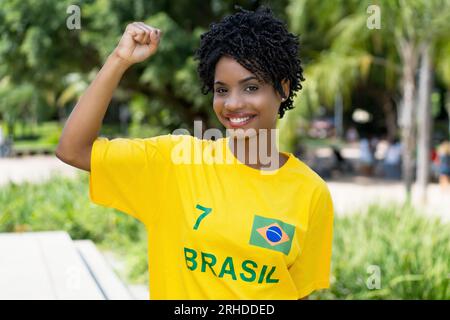 Excited young woman from Brazil with yellow football jersey outdoors in summer Stock Photo