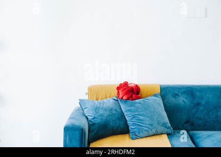 Blue sofa, 2 solid filled cushion, and a red cushion with a golden throw against white wall as background Stock Photo