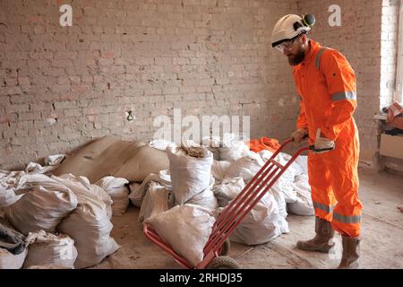 Construction worker transferring garbage on site using hand trolley. Stock Photo