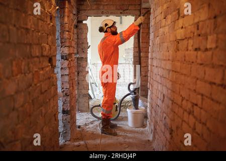 Constriction site worker cleaning brick wall with special vacuum cleaner after demolishing jobs. Stock Photo