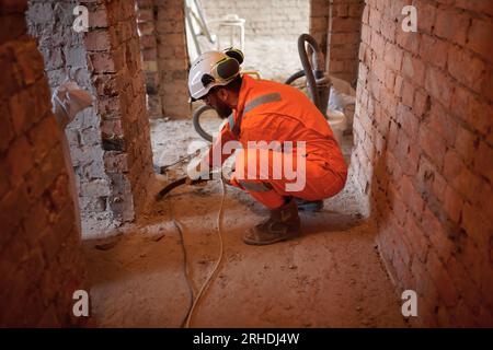 Constriction site worker cleaning concrete floor with special vacuum cleaner after demolishing jobs. Stock Photo