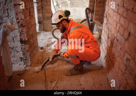 Constriction site worker cleaning concrete floor with special vacuum cleaner after demolishing jobs. Stock Photo