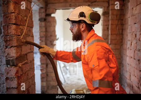 Close up of constriction site worker cleaning brick wall with special vacuum cleaner. Stock Photo