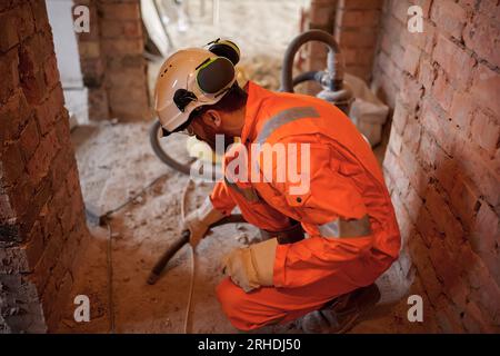 Close up of constriction site worker cleaning concrete floor with vacuum cleaner after demolishing jobs. Stock Photo