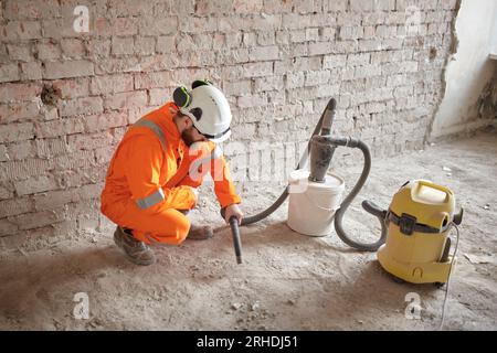 Male constriction site worker cleaning concrete floor from dust with special vacuum cleaner after demolishing jobs. Stock Photo