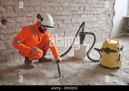 Male constriction site worker cleaning concrete floor from dust with vacuum cleaner after demolishing jobs. Stock Photo