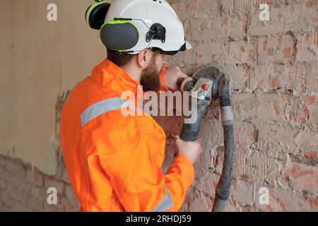 Construction worker grinding brick  wall using grinding machine with vacuum cleaner attached. Stock Photo