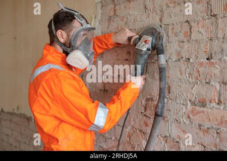Construction worker grinding brick  wall using grinding machine with suction hose attached. Stock Photo
