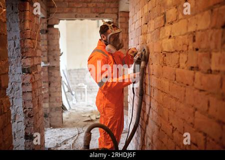 Construction worker cleaning brick  wall using grinding machine with vacuum cleaner attached. Stock Photo
