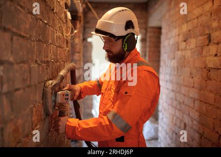 Construction worker grinding brick  wall using grinding machine with vacuum hose attached. No dust construction technology. Stock Photo