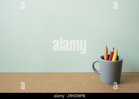 Colored pencils in gray holder on brown desk. mint green wall background. copy space Stock Photo