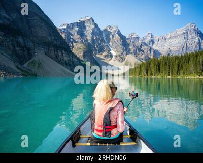 Woman taking a selfie in Canoe, Moraine Lake during summer in  Banff National Park, Canadian Rockies, Alberta, Canada.  Banff National Park, Alberta, Stock Photo