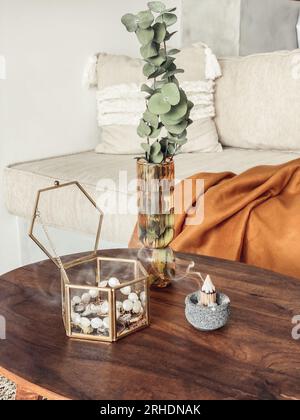 Glass vase with with eucalyptus leaves, jewelry box and incense stick on the coffee table in the living room near sofa Stock Photo