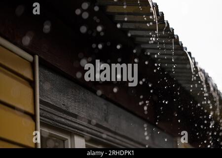 rainwater flows down from the roof of the house during the rain. raindrops dripping from the roof Stock Photo