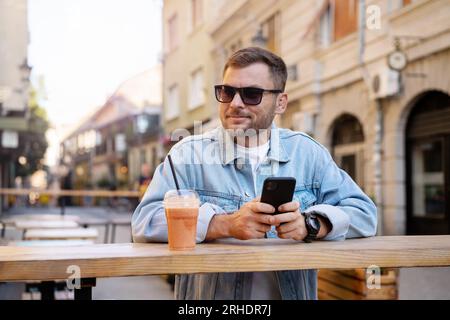 Urban weekends lifestyle, man using his cell phone and drinking smoothies in sidewalk cafe in old European town. Stock Photo