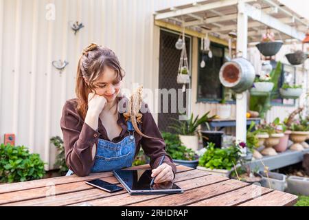 Happy young woman sitting at picnic bench in garden with pet lizards working on tablet laptop Stock Photo