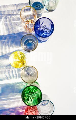 Line of brightly coloured glasses reflecting and bending light in bright sunlight on white table Stock Photo