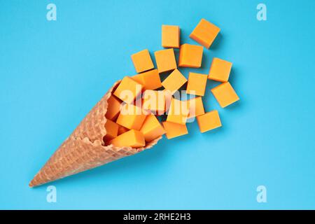 Waffle Cone with Yellow Cheese Cubes on blue background close-up Stock Photo
