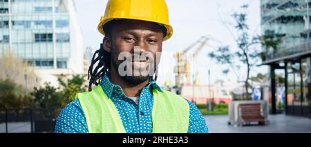banner of man with beard and dreadlocks of african ethnicity builder engineer and safety helmet, standing outdoors smiling with smile and very positiv Stock Photo