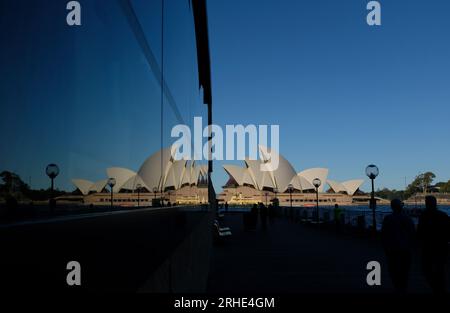 Sydney Opera House and a mirror image reflection of the Opera House Sails with a broad expanse of clear blue Australian sky, and people in silhouette Stock Photo