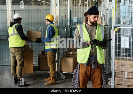 Young serious male engineer in reflective jacket looking at tablet screen while networking or looking through information in database Stock Photo