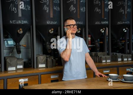 Cheerful barista talking on mobile phone in coffee shop, bartender coffeemaker at his workplace, Stock Photo