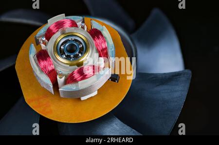 Close-up of electric motor stator with electronic coils and ball bearing. Red copper wire winding of computer fan electromotor on rotor plastic vanes. Stock Photo