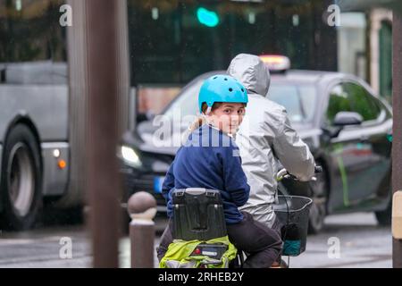 15 May 2023 Paris France. A girl and her father on bike commute home on a rainy unban street in Paris Stock Photo